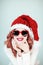 Santas little helper. Beautiful happy young woman with a santa claus hat, perfect make up, red lipstick, and heart shape sun glass