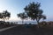 Santorini, black pebble beach of Perivolos at sunrise. Wooden walkway to the sea, two olive trees and under them a blue table with