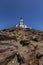 Santorini, Cape Akrotiri Lighthouse, a white lighthouse standing on a stone cliff. In the background a beautiful, azure, blue sky