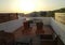 Santorini, Greece: Tables and resting chairs on big terrace roof balcony with a beautiful romantic view of hills, sea and sunset