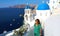 Santorini travel tourist woman visiting famous white village with blue domes Oia, Greece. Girl in green dress and sunglasses