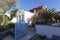 Santorini, a white Greek house with a blue wooden garden, the first floor is covered with blooming various flowers, a palm tree