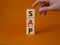 SAP - Systems Applications Products. Wooden cubes with word SAP. Businessman hand. Beautiful orange background. Business and