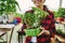 Saplings of plants with soil grown in plastic container in the hands of a smiling woman standing in an old home country greenhouse