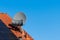 Satellite dish on the roof of a house covered with terracotta tiles. Solar panels on the roof. Blue sky