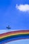 Satellite dish on top of the old building with rainbow stripes on building wall surface against blue sky