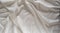 Satin crumpled fabric of light milky color, top view. Natural bed linen, sheets, abstract background of luxury fabric