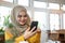 A satisfied Asian-muslim woman is using her smartphone while sitting in a coffee shop