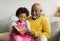 Satisfied black little kid and elderly man reading book with fairy tales on sofa in living room interior