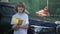 Satisfied Caucasian cute boy smiling looking at camera standing with car wash sponge as blurred man checking clean hood