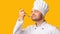 Satisfied Chef Man Tasting Delicious Dish Holding Spoon, Yellow Background