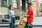 Satisfied customer receives online order. Girl takes cardboard parcel from courier with backpack and bicycle