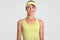 Satisfied cute young active female tennis player, dressed in yellow court cap and t shirt, has healthy skin, poses against white s