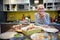 Satisfied elderly female waiting guests with ready food on a table