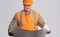 Satisfied engineer in hard hat looking in opened paper project in hands on grey studio background, construction industry