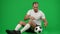 Satisfied excited Caucasian sportsman gesturing yes sitting with football ball at chromakey background. Portrait of