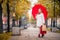 Satisfied girl with red umbrella and shopping packages goes on autumn city street