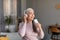 Satisfied glad european senior woman with gray hair in wireless headphones enjoys music and sings song