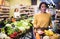 Satisfied hispanic woman with shopping trolley in supermarket