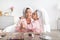 Satisfied korean teenage girl kissing young lady in pink pajamas and towel on head at table with cosmetics