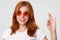 Satisfied lovely Caucasian female in stylish shades, shows okay gesture, aprroves this good idea or plan, smiles pleasantly, shows
