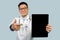 Satisfied mature chinese male therapist in white coat, glasses pointing on tablet with empty screen