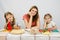 Satisfied mother with two daughters sitting resting his head in his hands at the table with products for pizza