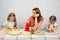 Satisfied mother watching her little daughter to help her cut products at kitchen table