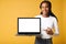 Satisfied multiracial woman advertising new computer app isolated on yellow background, mock-up. Positive smiling female