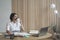 Satisfied positive Spanish female entrepreneur in wireless headset drinking coffee in office
