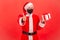 Satisfied santa claus in protective mask on face holding gift box with red bow and showing thumbs up, likes holidays presents