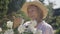 Satisfied senior female florist admiring beauty of white blossom on bush branch in sunlight. Portrait of positive