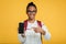 Satisfied smart adolescent black lady pupil in glasses with backpack shows finger at smartphone with blank screen