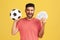 Satisfied smiling man with beard in striped t-shirt holding soccer ball and fan of dollar banknotes, sports betting, big win