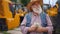 Satisfied smiling senior man counting cash money standing outdoors with yellow tractors at background. Portrait of happy