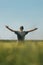 Satisfied successful farmer raising hands in victorious pose in unripe barley crops field on sunny spring day. Rear view of farm