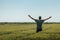 Satisfied successful farmer raising hands in victorious pose in unripe barley crops field on sunny spring day. Rear view of farm