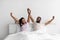 Satisfied young african american guy and lady raise hands, stretching body on bed in bedroom interior