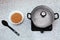 Saucepan on a small electric stove with a steamed lid. On the table there is a bowl with buckwheat groats and a spoon.