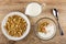 Saucer with muesli, bowl with granola and yogurt, jug of yogurt, spoon on wooden table. Top view