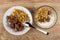 Saucer with porous chocolate and granola, bowl with muesli, yogurt, chocolate, spoon on table. Top view