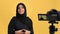 Saudi woman in hijab talking shoot video vlog blog use camera screen posing isolated orange studio