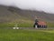 Saurbaejarkirkja black wooden red roof church on green grass field, steep hills in fog, Raudisandur, iceland west fjords