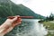 Sausage in the hands of a man on the background of a lake in the mountains. Nature and snack sausage. Food on a hike