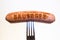 Sausage with an inscription pinned on a fork, on a white background.