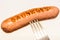 Sausage with an inscription pinned on a fork, on a white background.