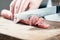 Sausage, knife, hands of woman, thick pieces, wooden plank, knife in female hands, woman cuts the sausage