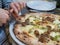 Sausage pizza being cut with traditional scissors on table being cut by woman