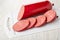 Sausage in polyethylene pack, slices of sausage on cutting board on wooden table