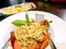 Sausage spaghetti in Thai style on white ceramic plate with spoon and fork and garlic bread in aluminium plate